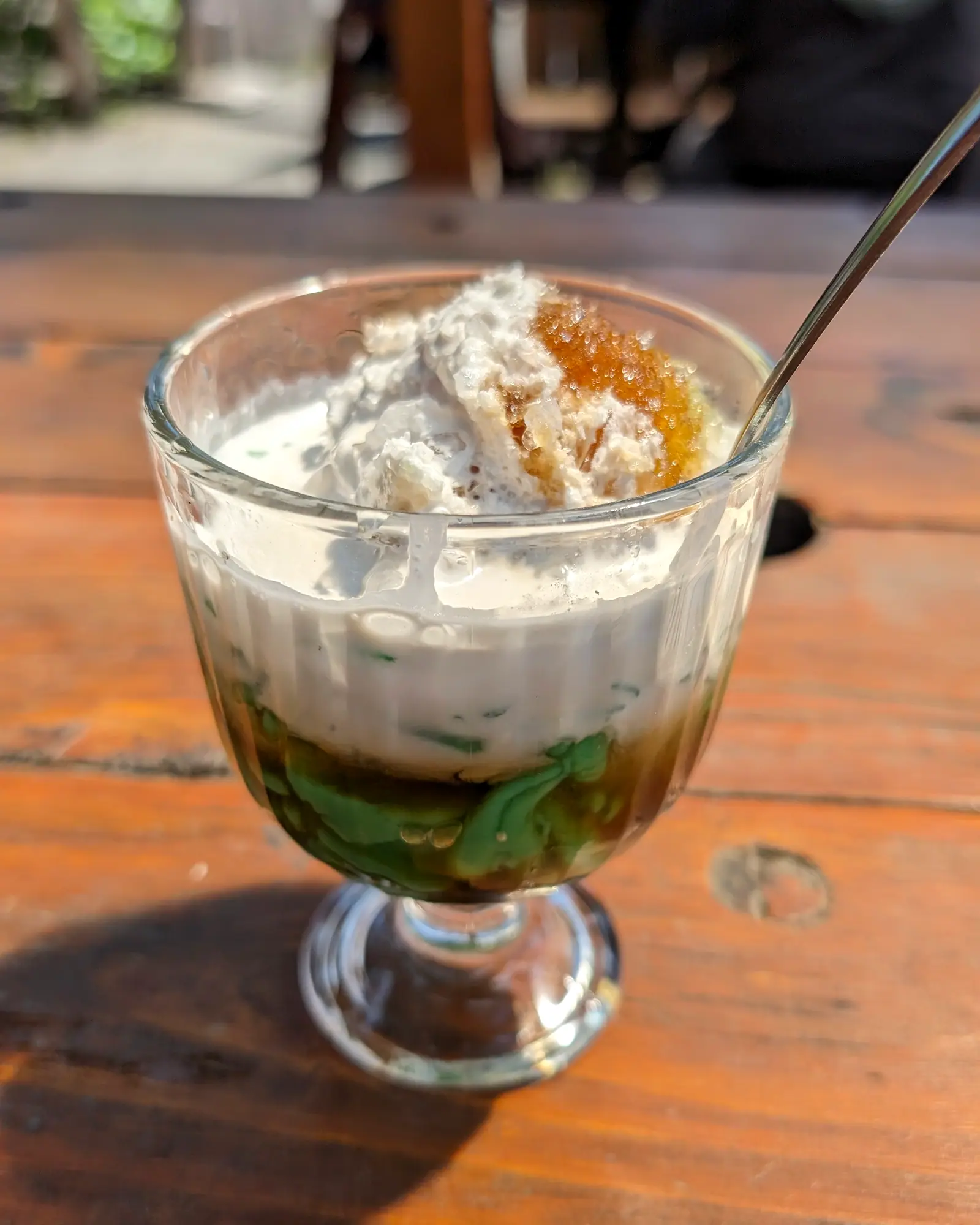Es cendol in a footed glass, green rice-flour jelly and dark palm sugar syrup layered under coconut milk