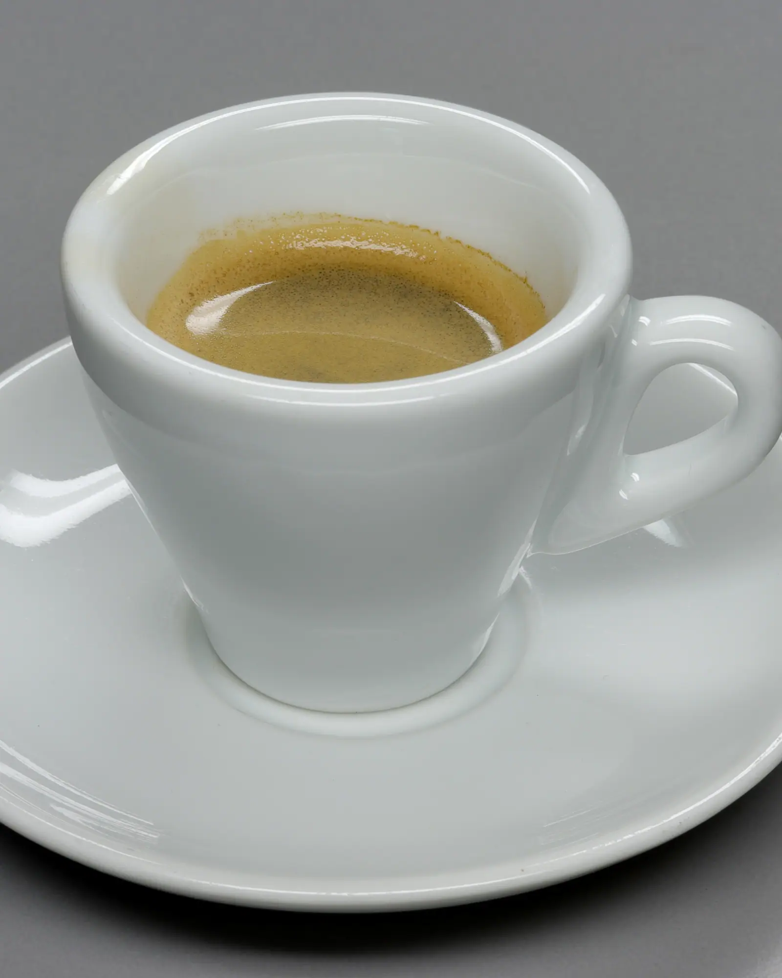 A white espresso cup with crema-topped espresso, on a matching saucer