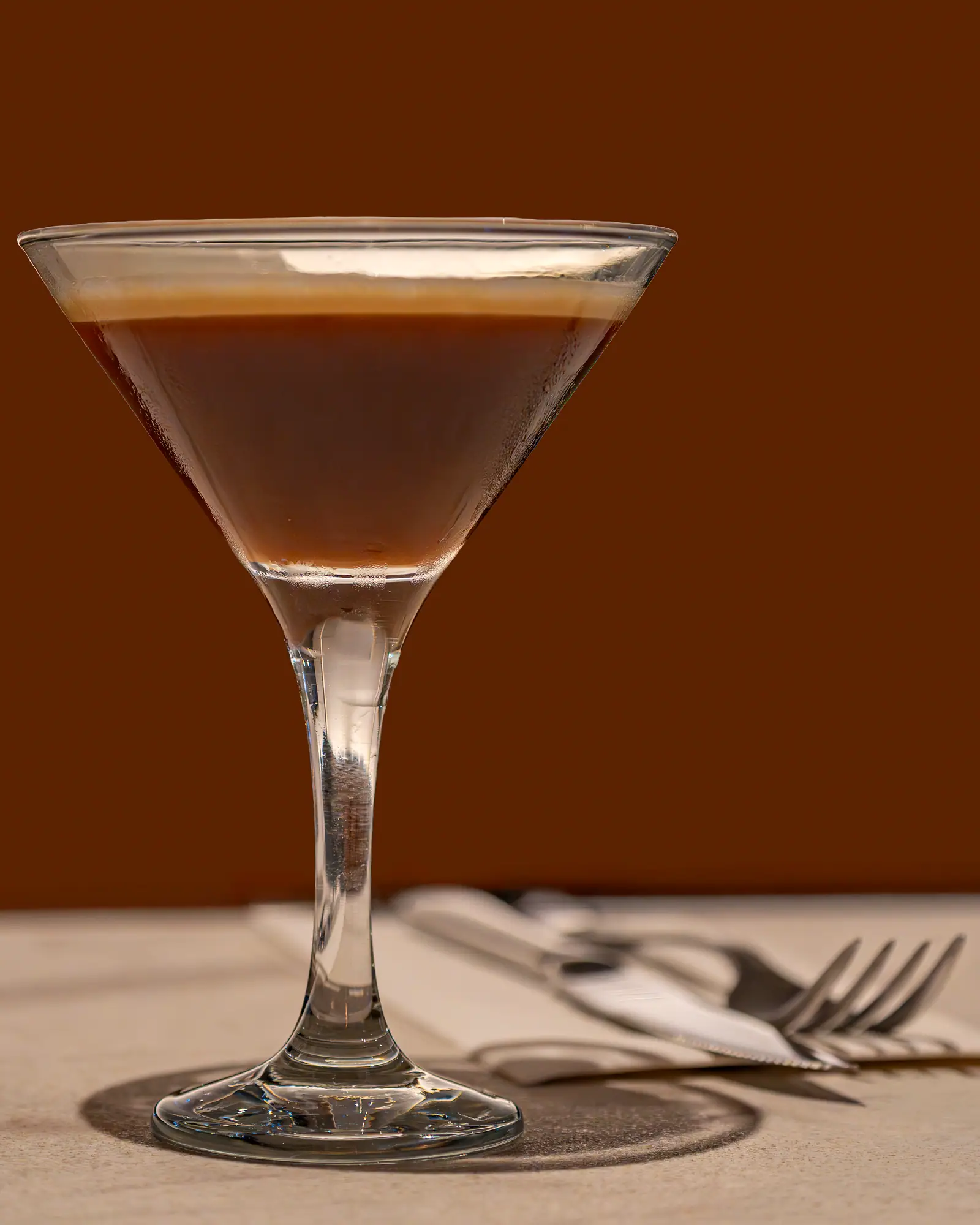 An Espresso Martini in a martini glass, dark coffee liqueur under a tan crema-coloured foam