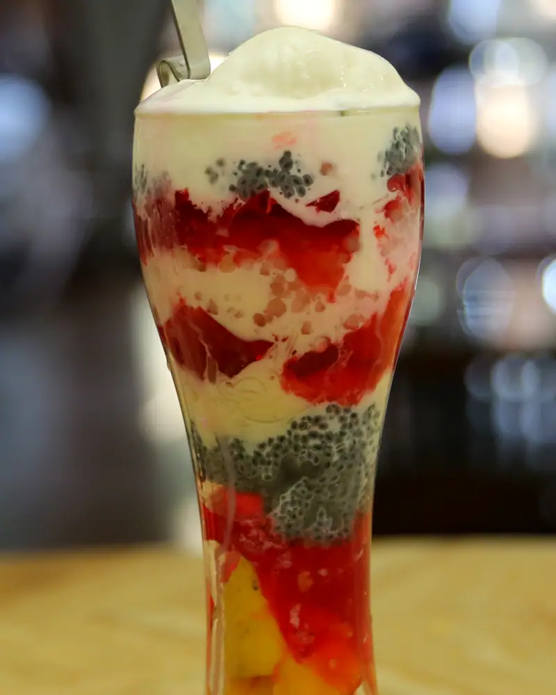 Layered falooda in a tall glass: red syrup, basil seeds and vermicelli under whipped cream