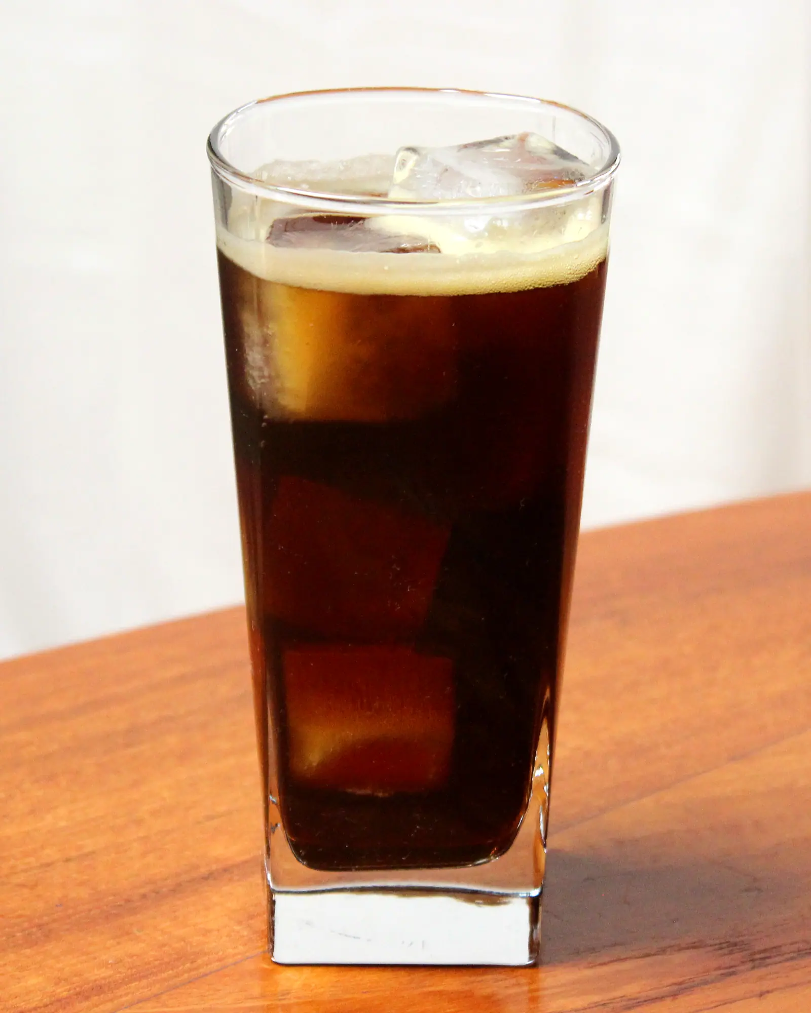 A dark Fernet con Coca in a tall glass over ice, on a wooden table