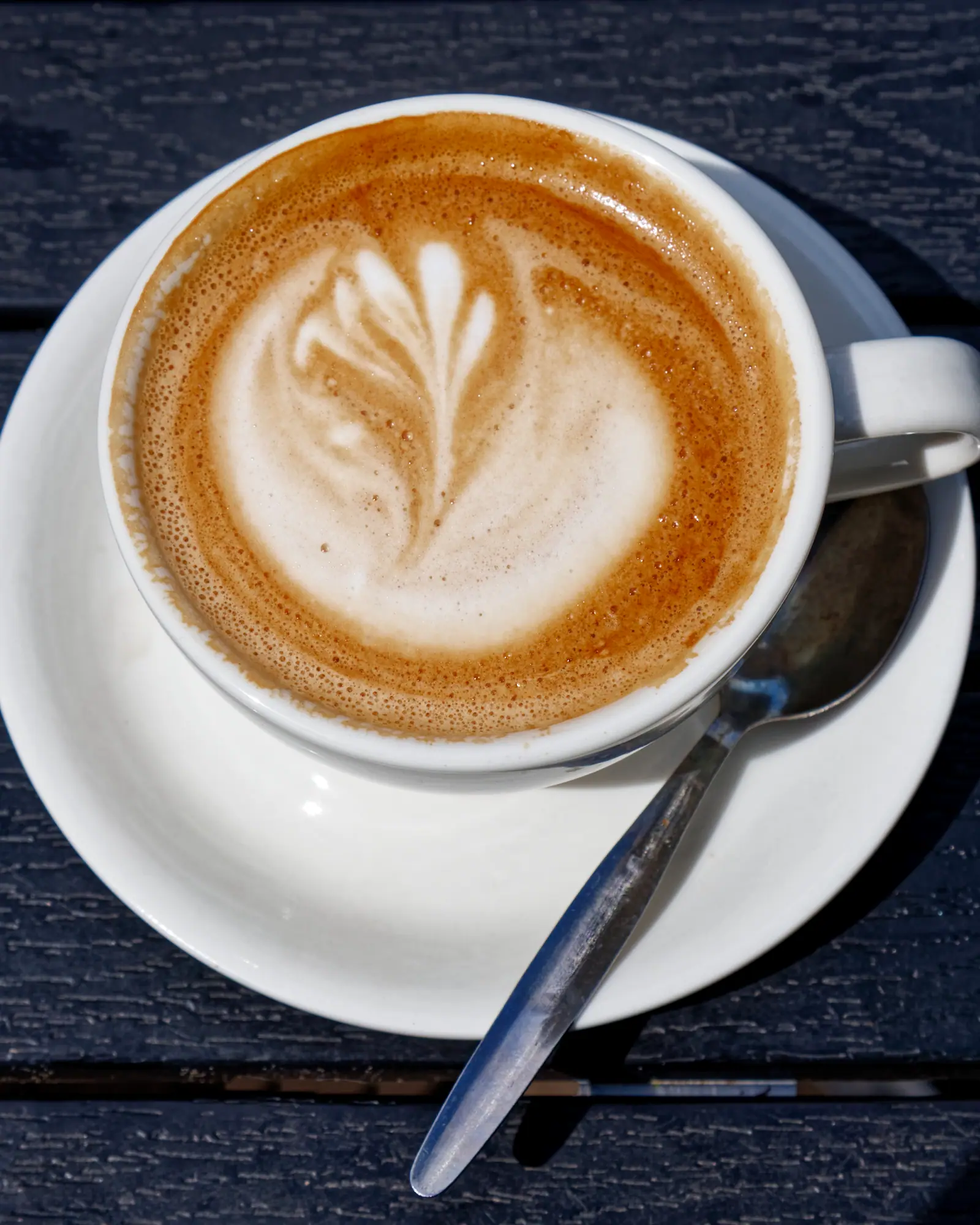 A flat white in a white cup, tulip-shaped latte art in the microfoam, on a matching saucer with a spoon