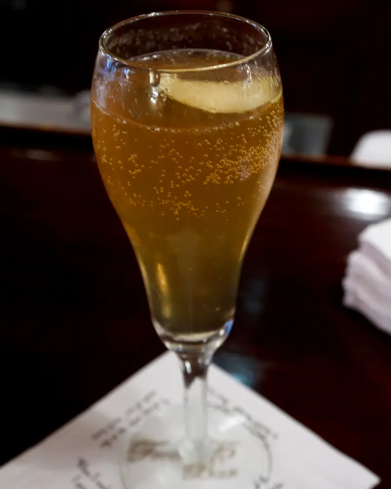 A French 75 served in a champagne flute, pale gold and effervescent, with a lemon twist