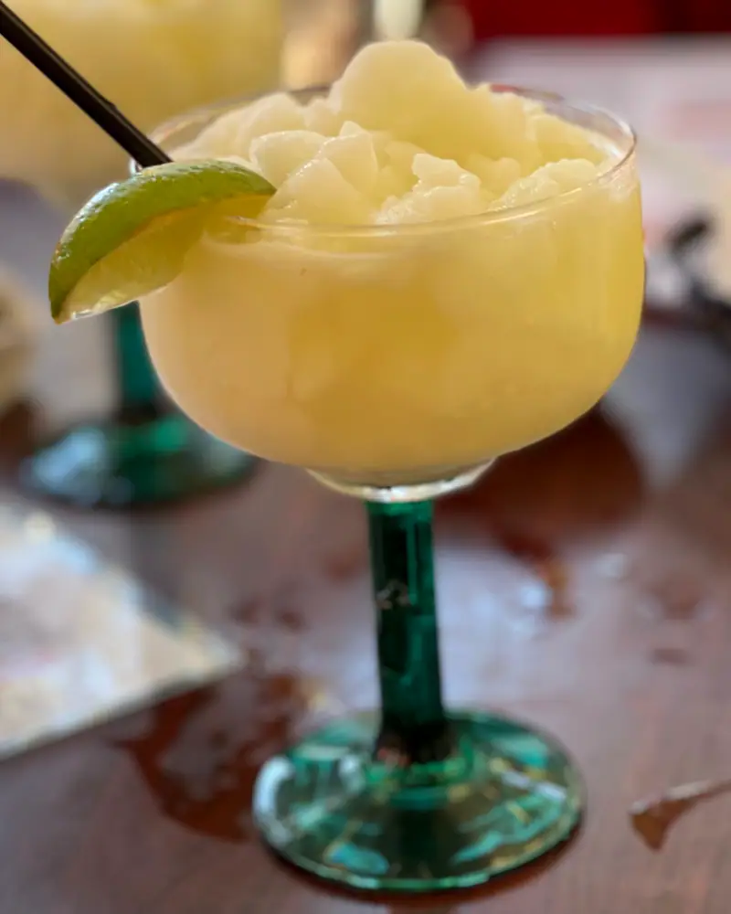 A frozen margarita with an icy, slushy texture, served in a margarita glass with a green stem and garnished with a lime wedge