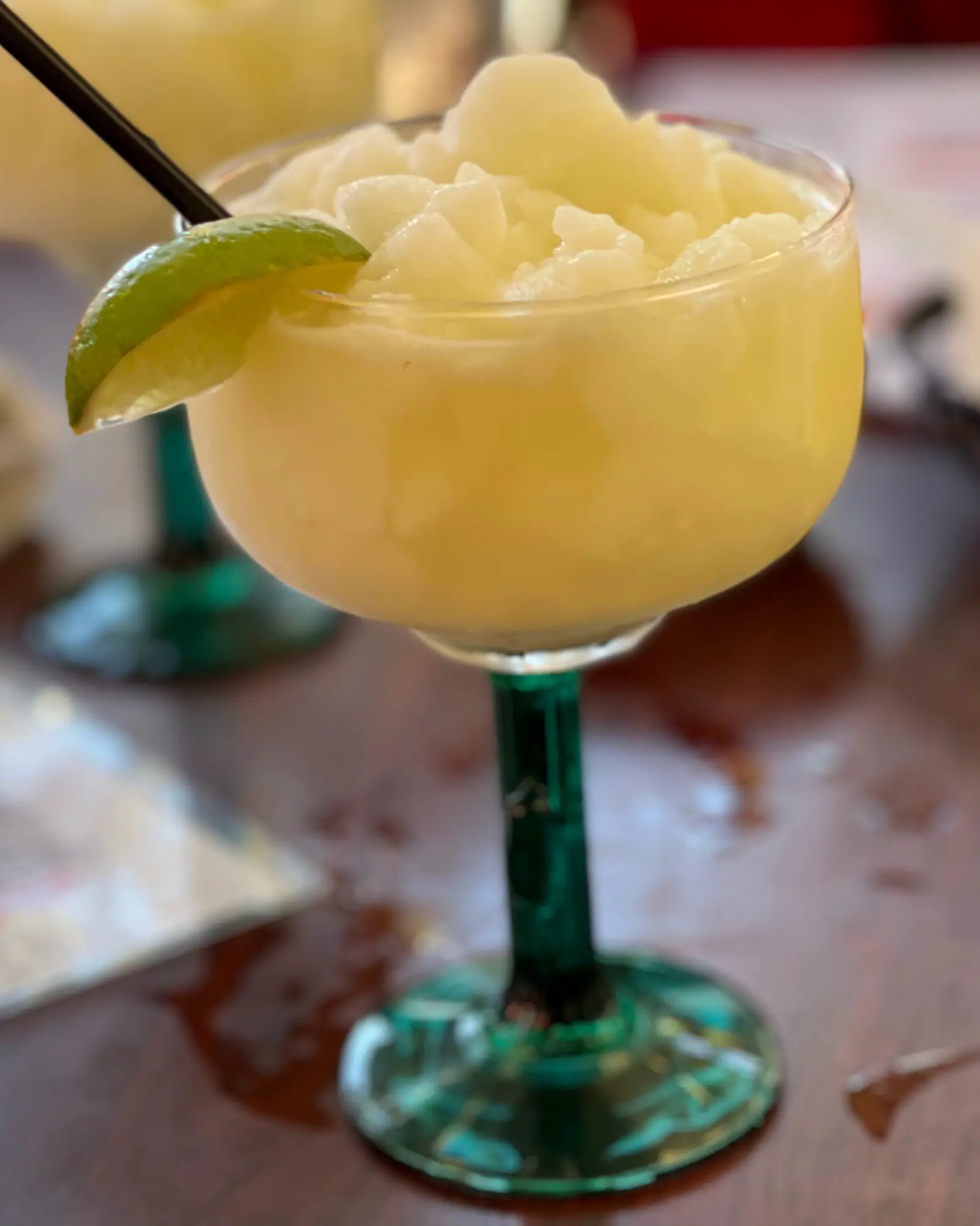 A frozen margarita with an icy, slushy texture, served in a margarita glass with a green stem and garnished with a lime wedge