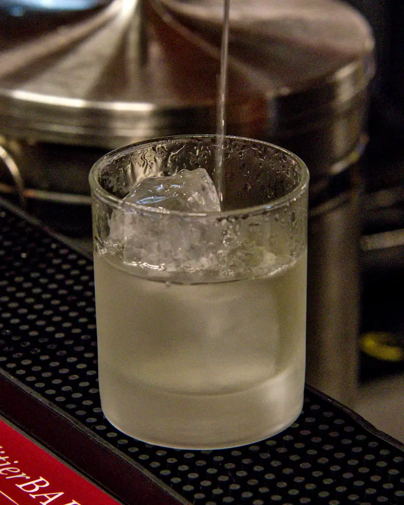A pale, clear Gimlet with ice poured into a rocks glass at a bar