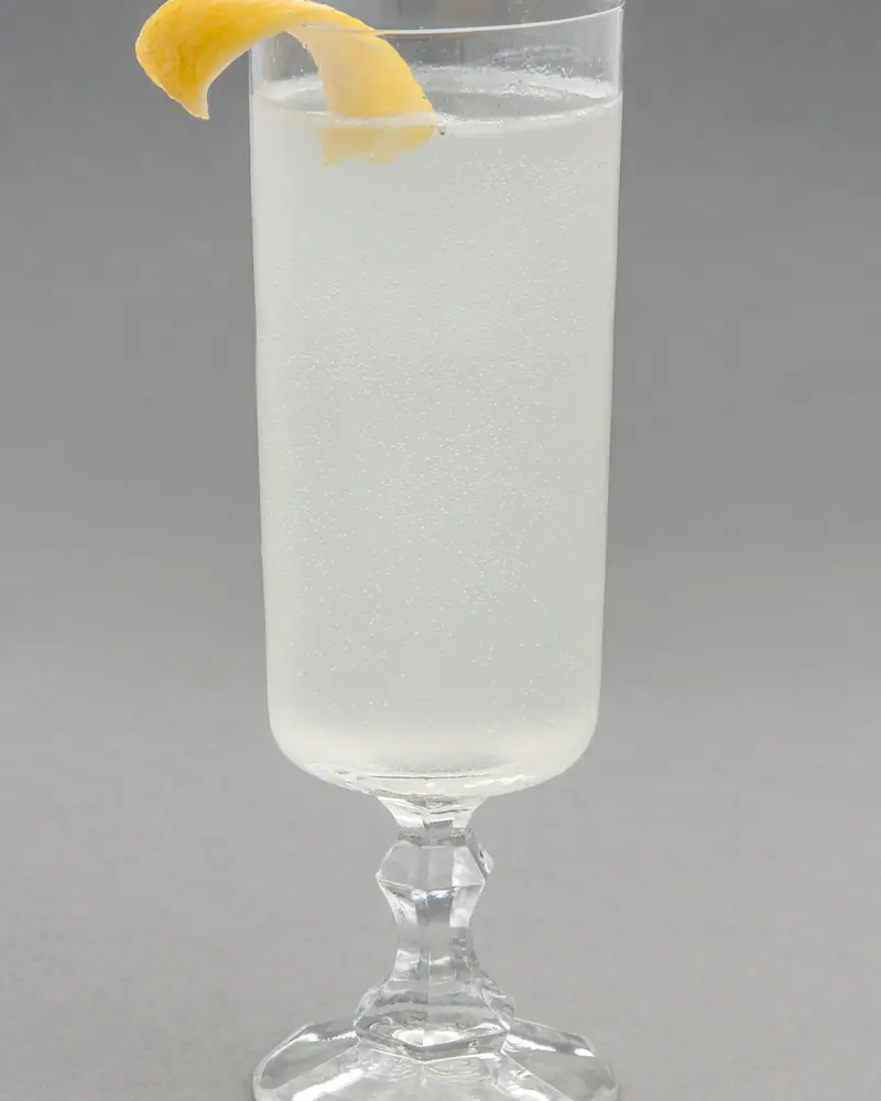 A clear, fizzy Gin Fizz in a tall stemmed glass, garnished with a curl of lemon peel