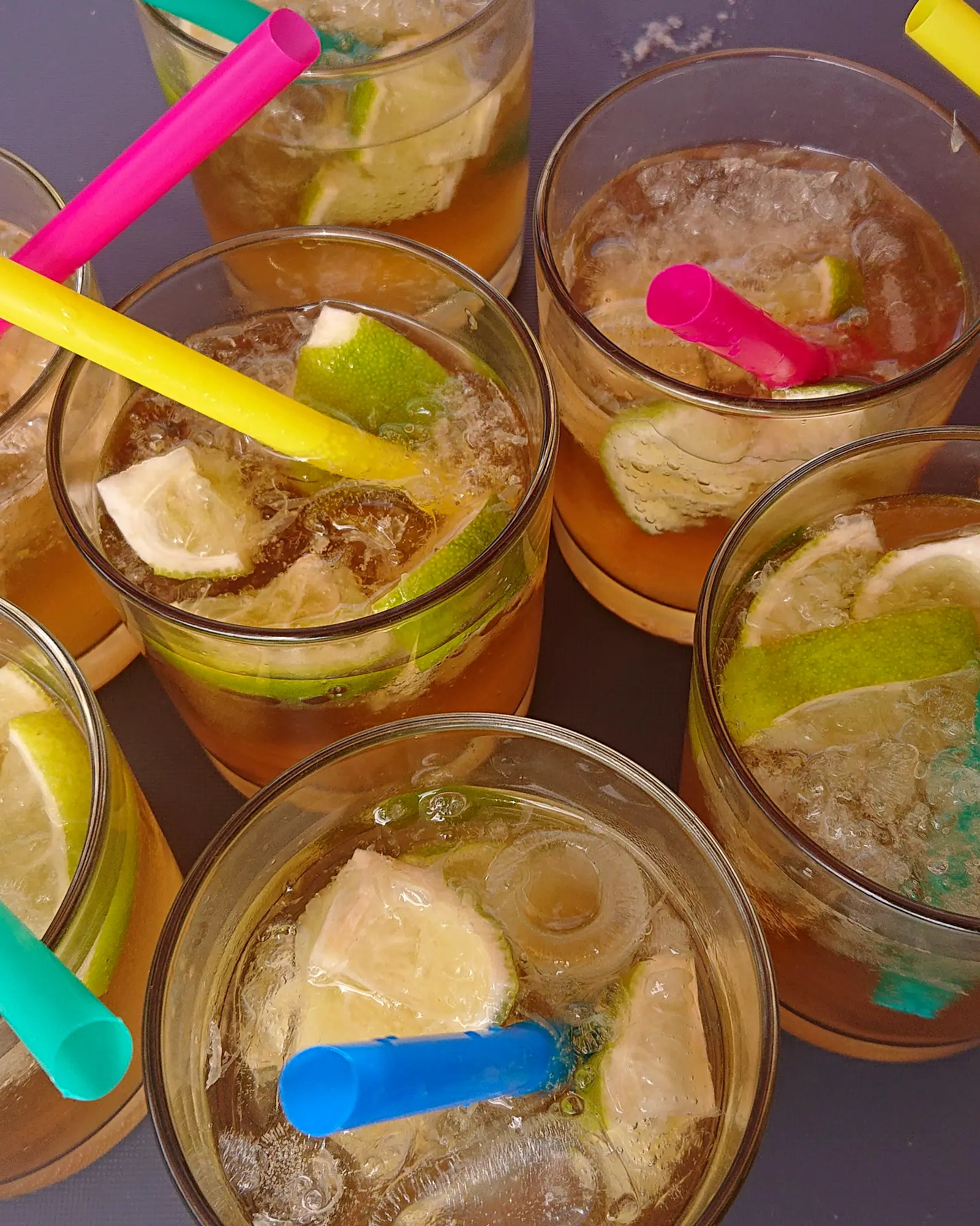 Amber ginger ale over ice in glasses garnished with lime wedges and colourful straws