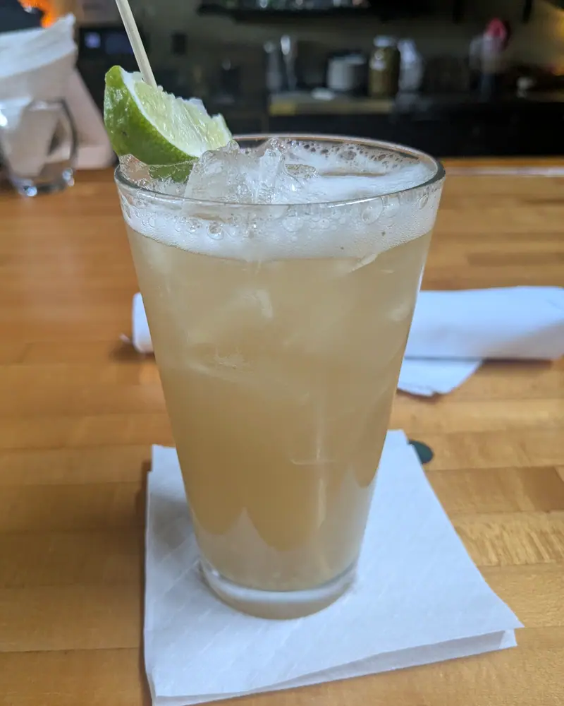 Cloudy, pale-amber homemade ginger beer over ice in a glass, garnished with a lime wheel