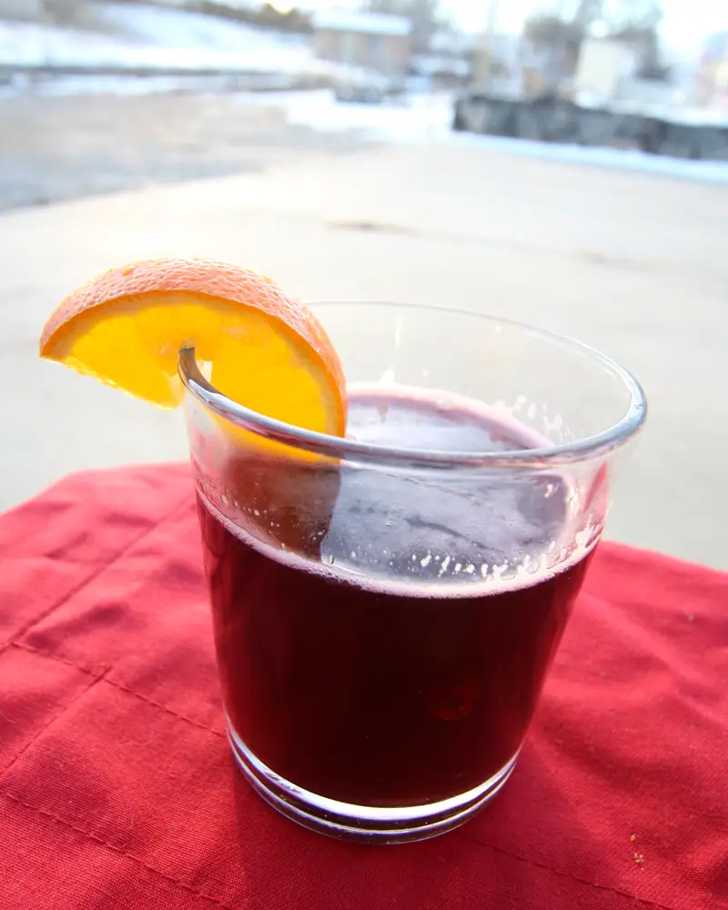 A glass of dark red glögg mulled wine with an orange slice at the rim