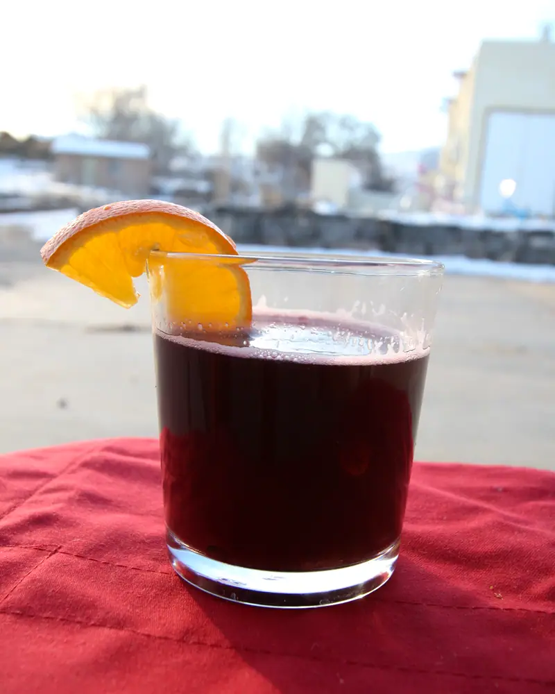 A glass of dark red Glühwein with an orange slice at the rim