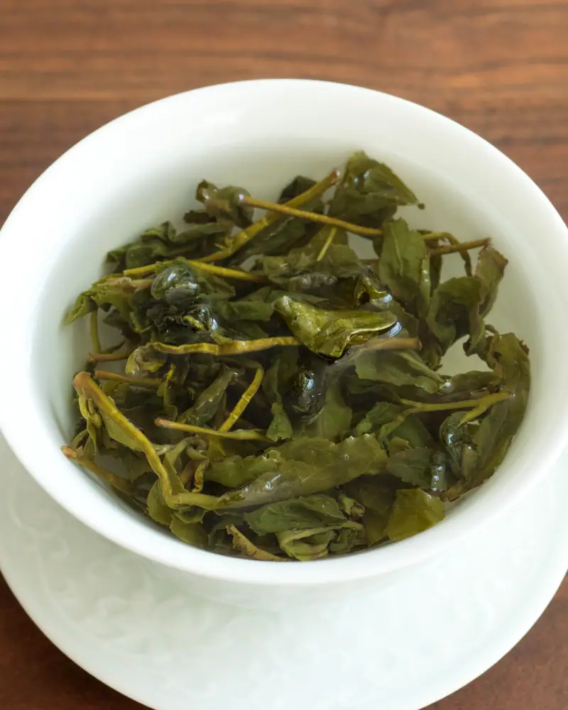 Unfurled green oolong leaves steeping in an open white gaiwan