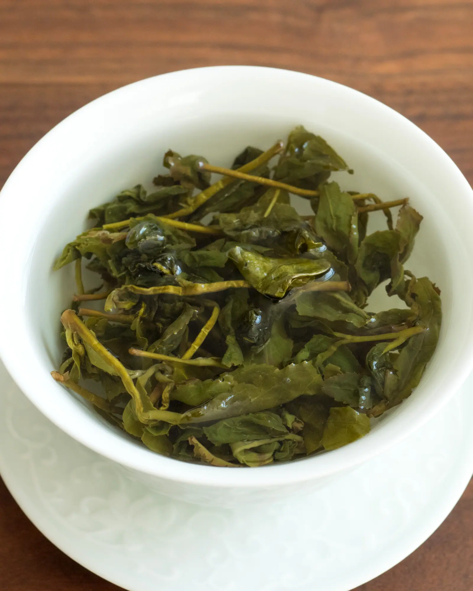 Unfurled green oolong leaves steeping in an open white gaiwan