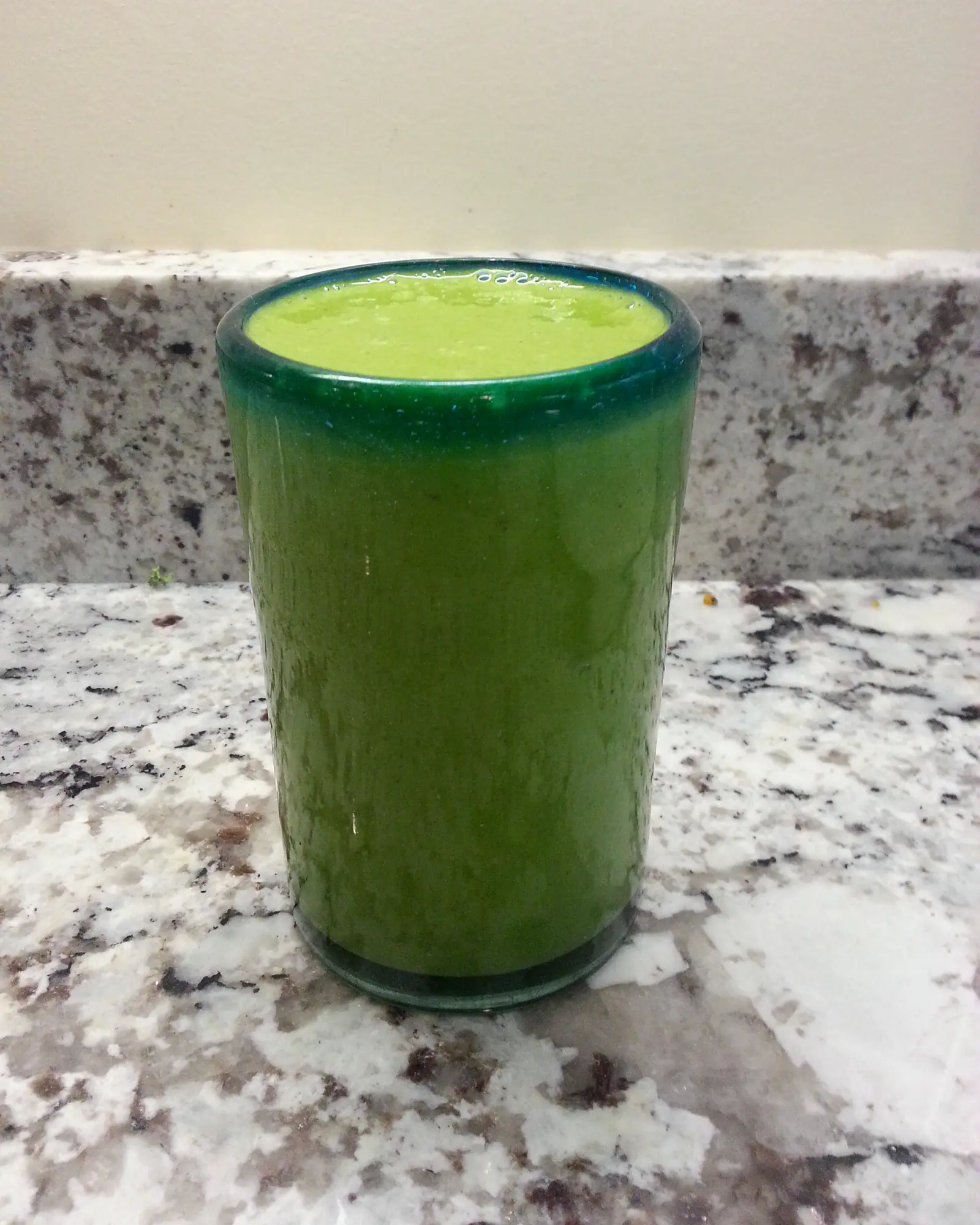 A glass of thick, dark green smoothie filling a plain tumbler, set on a granite counter