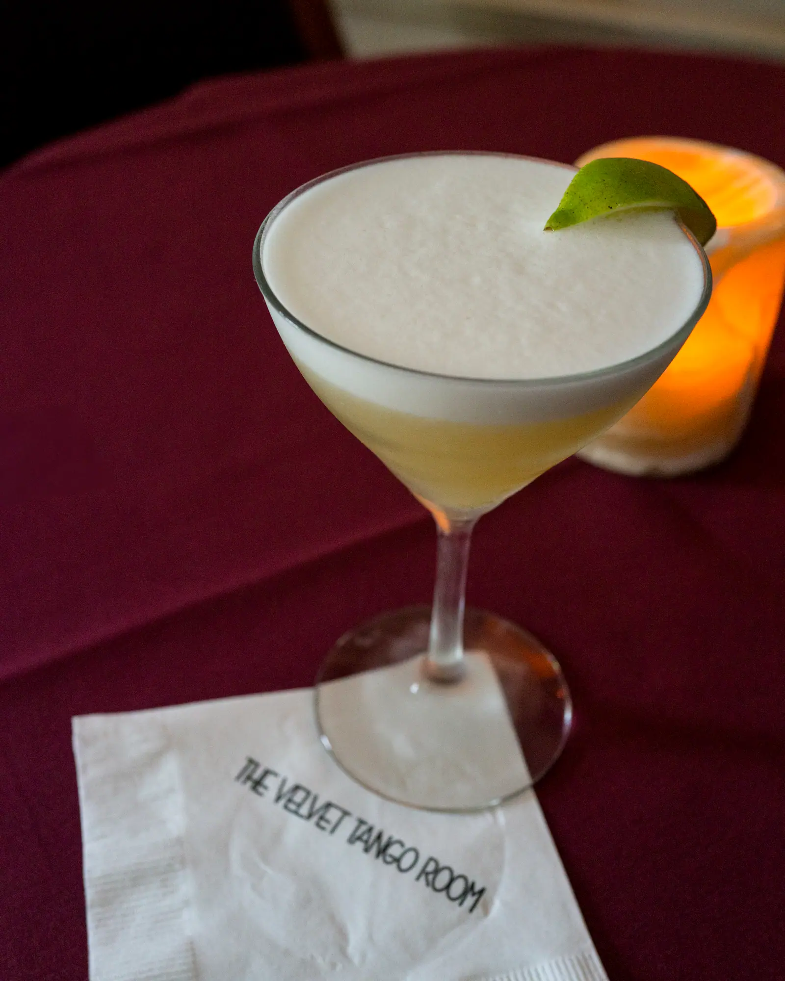 A Hemingway Daiquiri in a coupe, pale straw-coloured with a light foam, garnished with a lime wheel on the rim