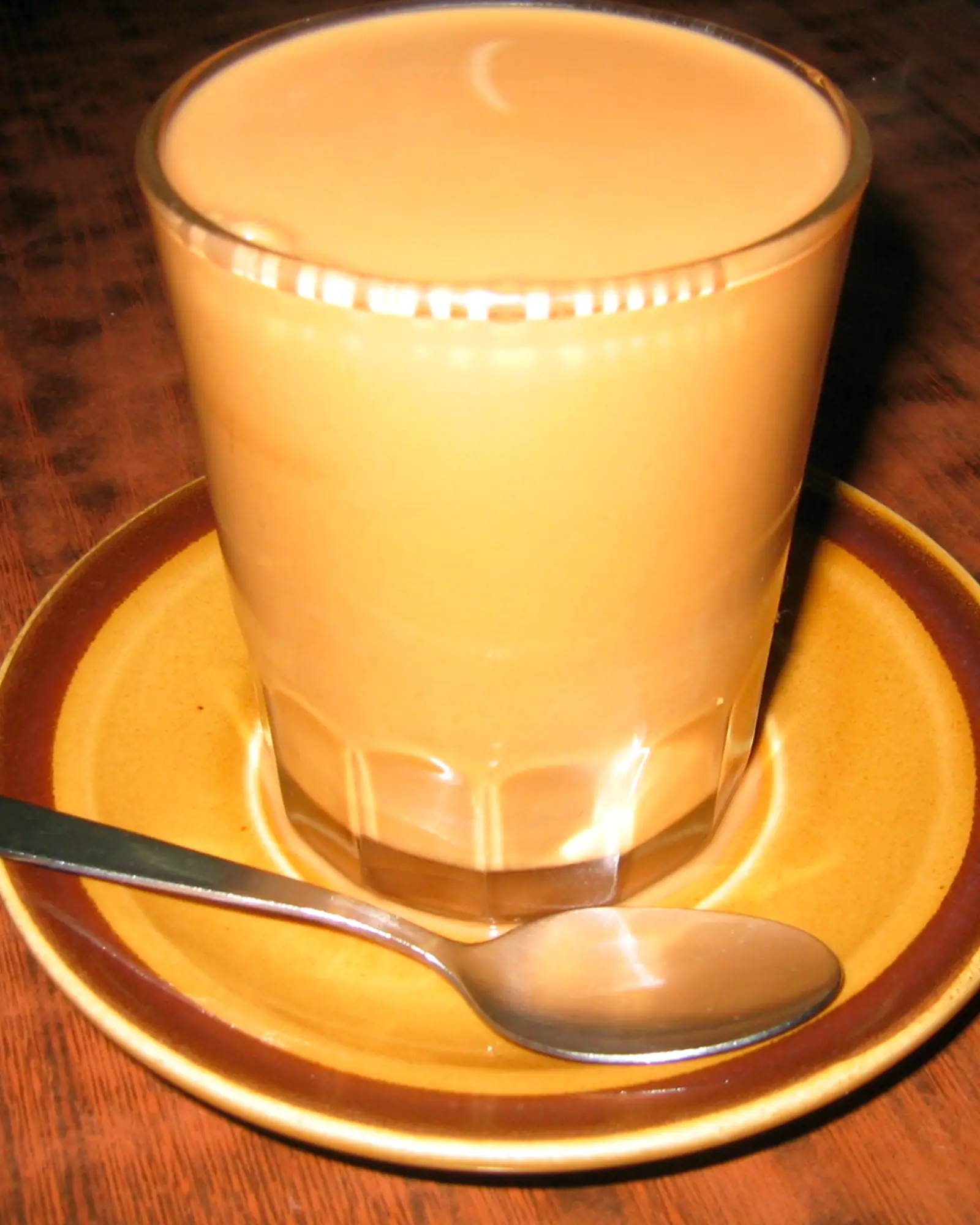 A glass of Hong Kong-style milk tea on a saucer with a spoon
