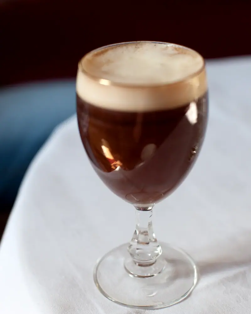 An Irish Coffee in a footed glass, dark coffee under a layer of pale cream