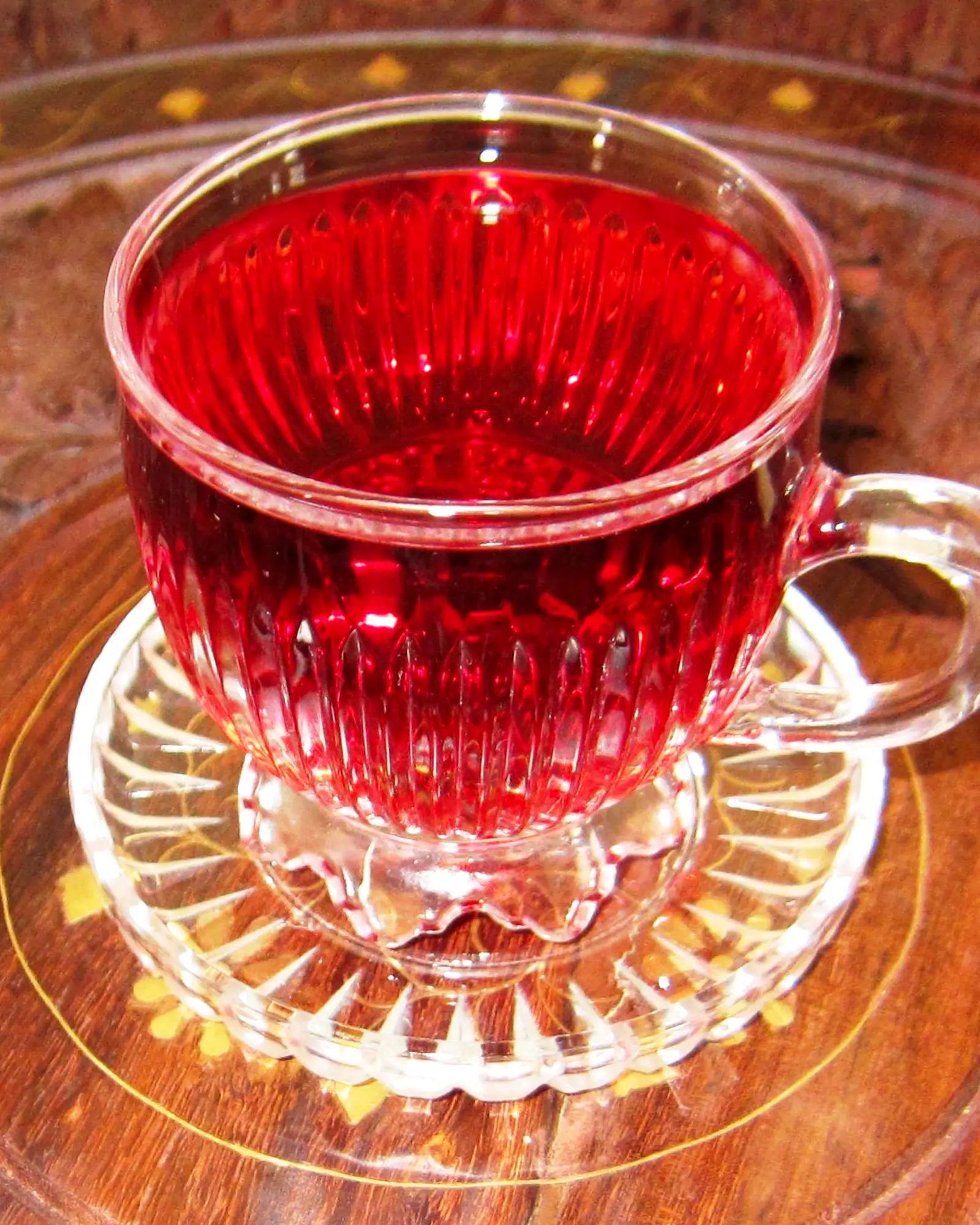 Deep red hibiscus infusion filling a glass teacup on a matching saucer