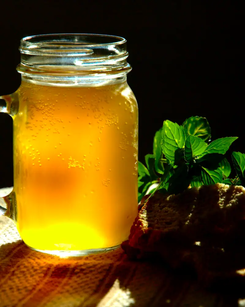 Amber kvass in a mason jar mug, lit warmly, with a sprig of fresh mint beside it