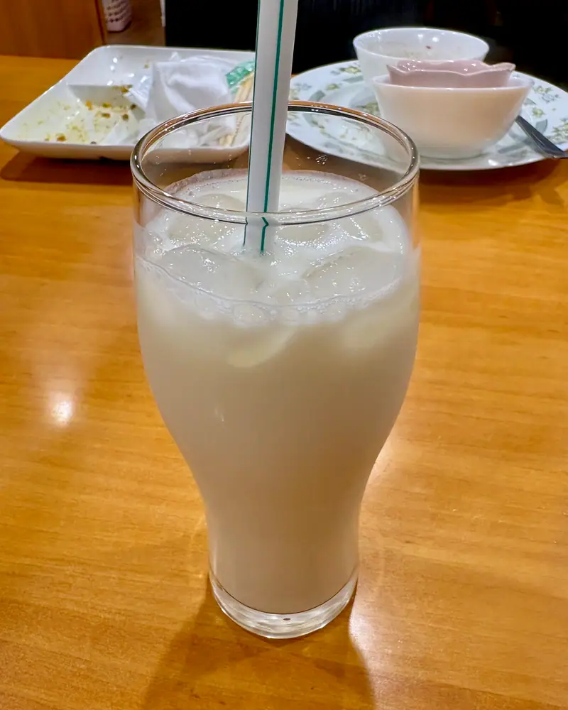 A tall glass of white, frothy plain lassi with a straw