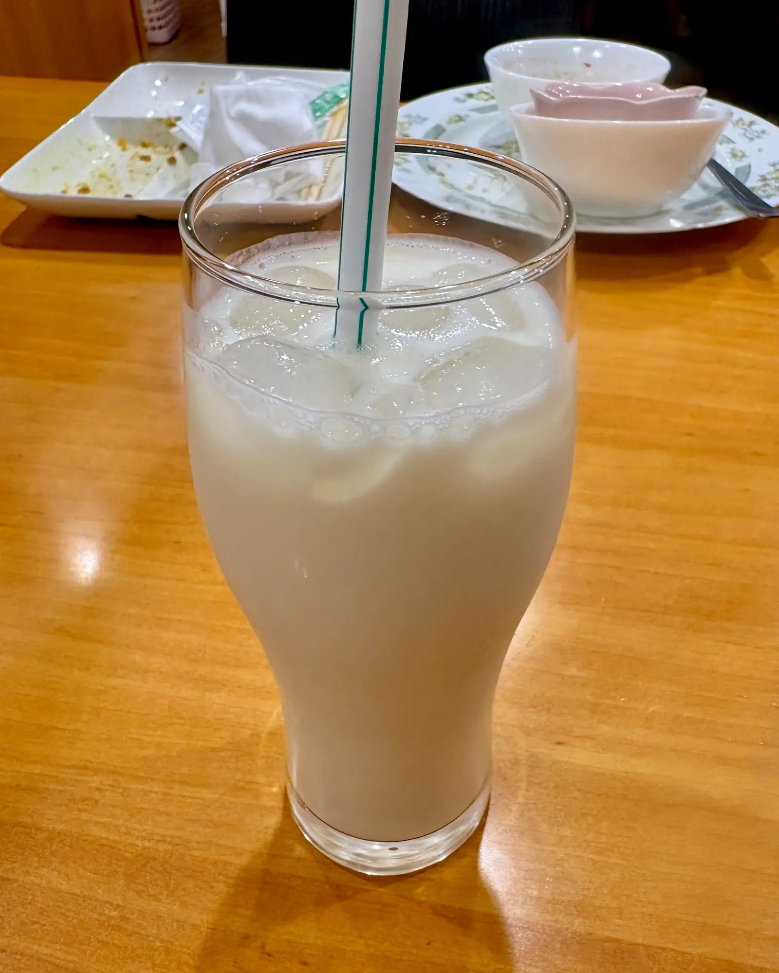 A tall glass of white, frothy plain lassi with a straw