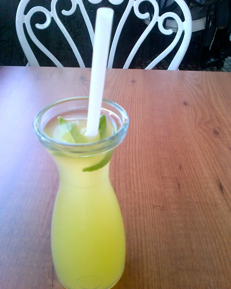 Pale yellow lemonade with a slice of lime in a small carafe with a straw