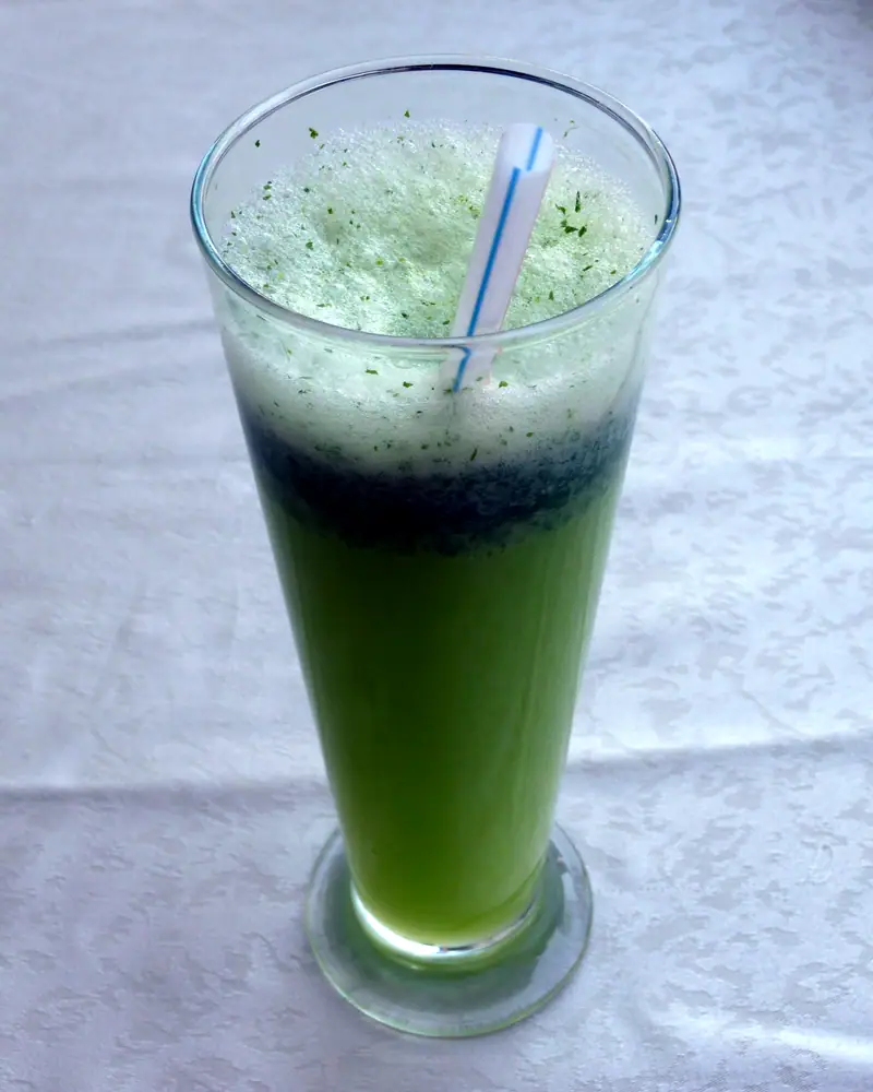 A tall glass of blended, bright green mint lemonade slush with a straw