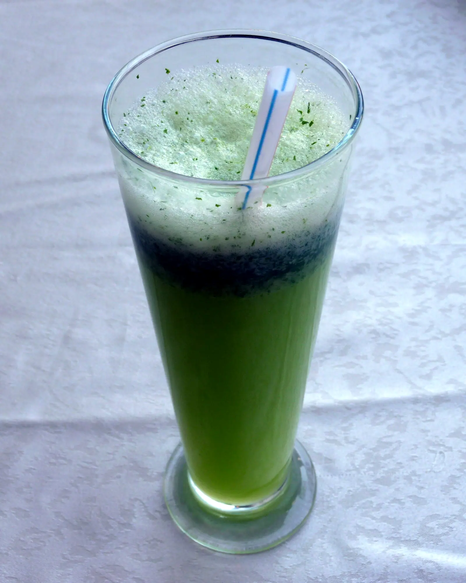 A tall glass of blended, bright green mint lemonade slush with a straw