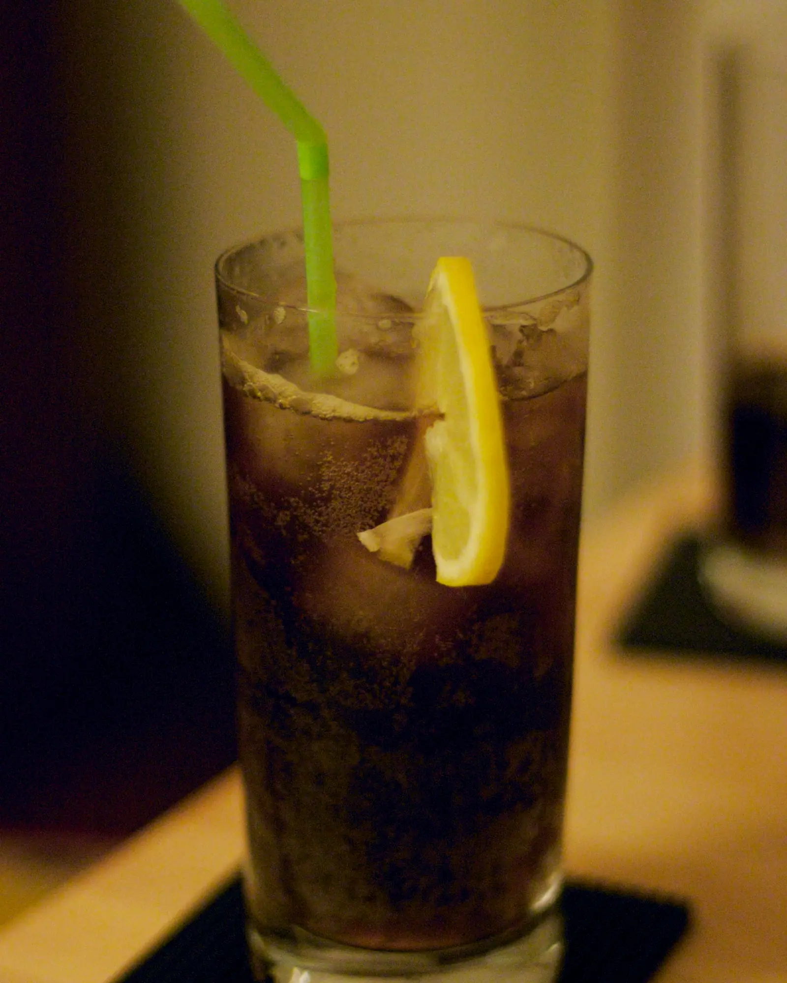 A Long Island Iced Tea in a tall glass over ice, garnished with a lemon wheel and a green straw