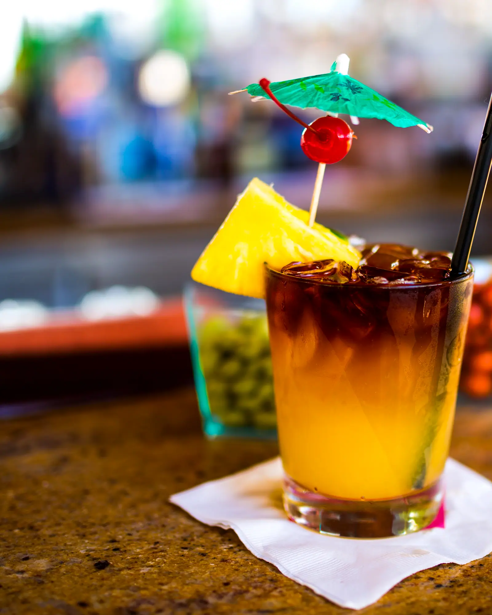 A Mai Tai in a rocks glass over crushed ice, dark rum floated over orange, garnished with a pineapple wedge, cherry and paper umbrella