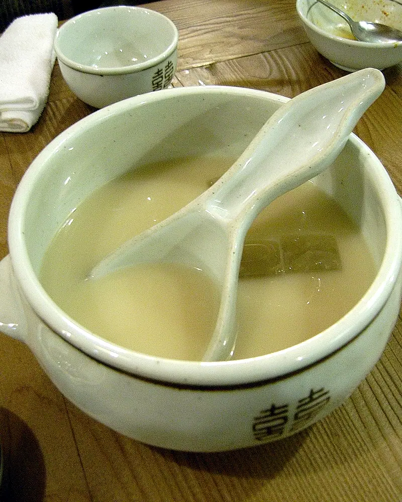Milky white makgeolli in a traditional ceramic bowl with a ladle, small cups beside it