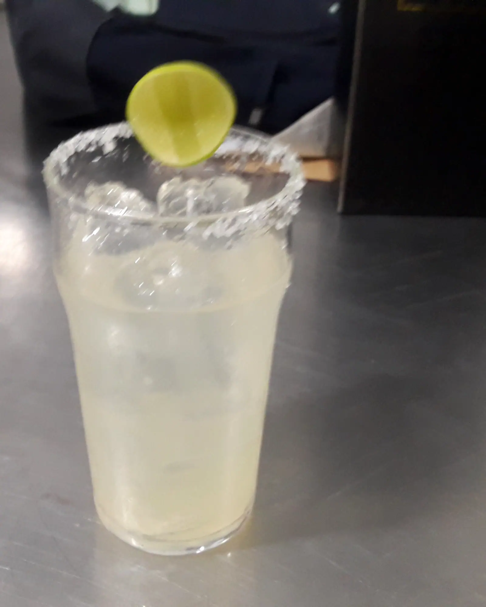 A pale, salt-rimmed Margarita over ice in a tall glass, garnished with a lime wheel