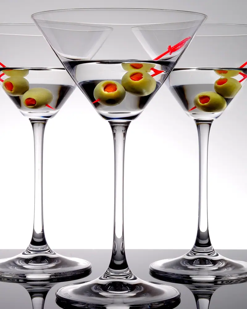 Several martinis in stemmed cocktail glasses, each garnished with green olives on a pick, against a plain white background