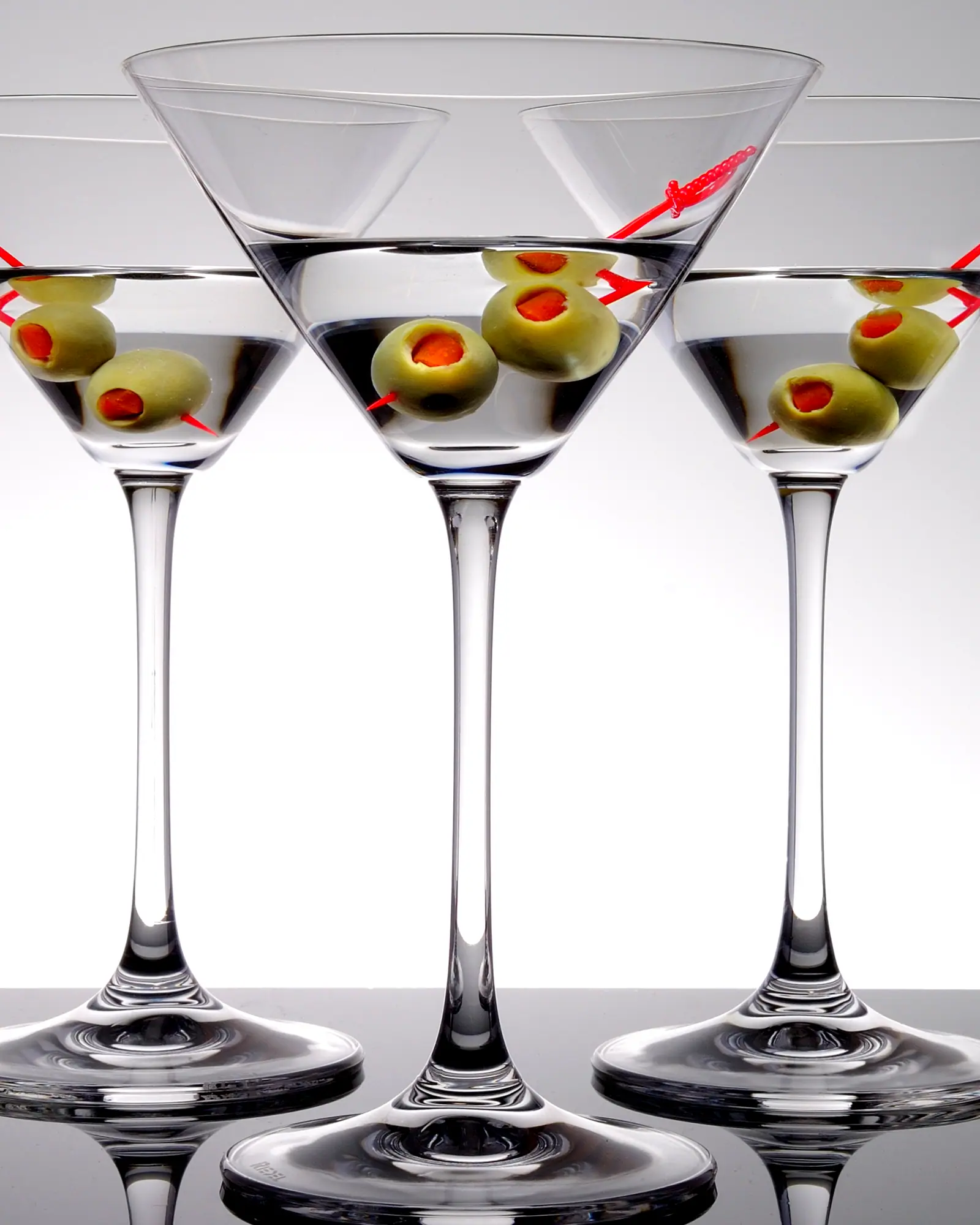 Several martinis in stemmed cocktail glasses, each garnished with green olives on a pick, against a plain white background