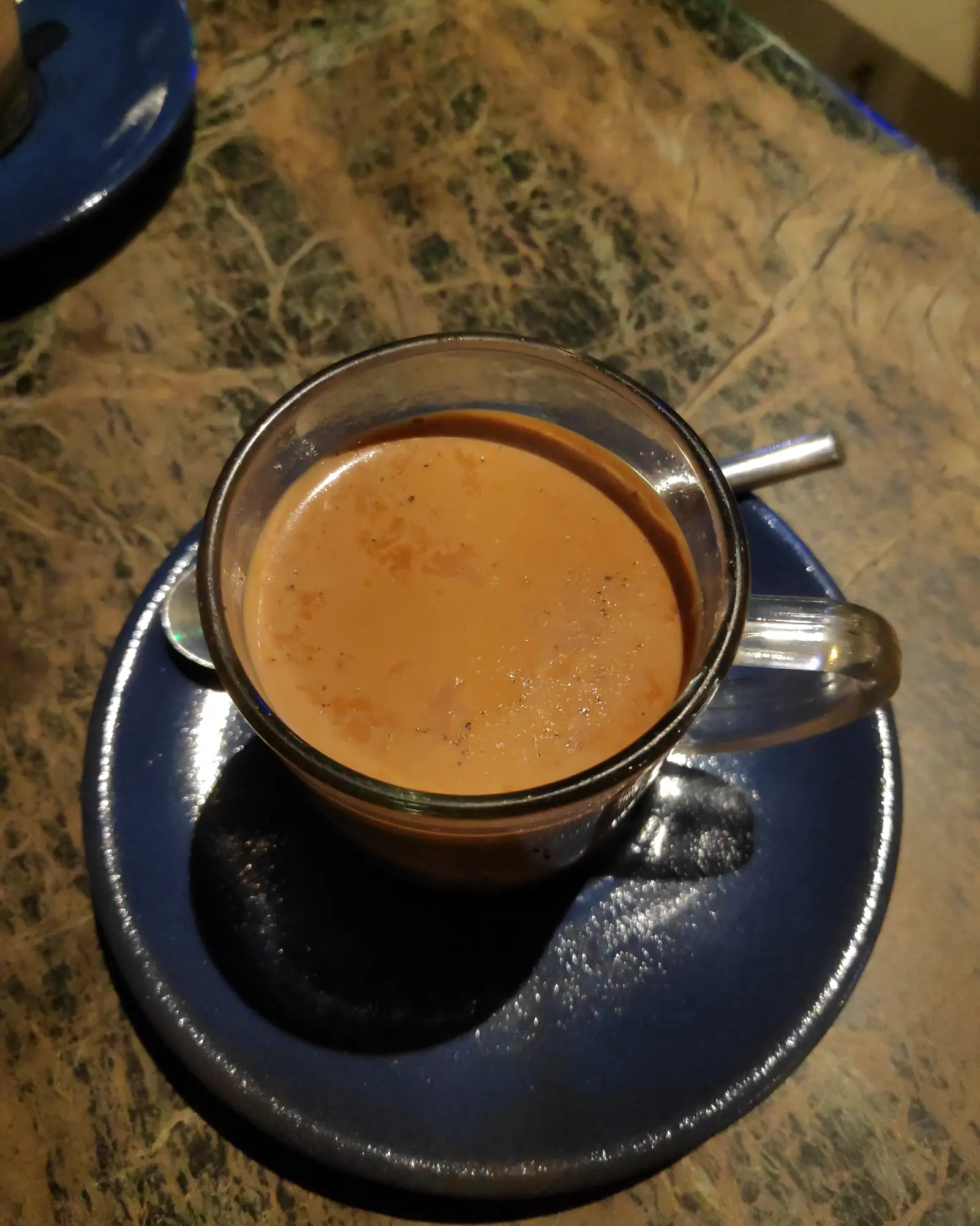 Overhead view of masala chai in a glass cup on a saucer, milky tan-coloured with a thin foam