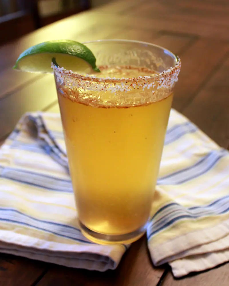 A Michelada in a pint glass with a chili-salt rim and a lime wedge garnish