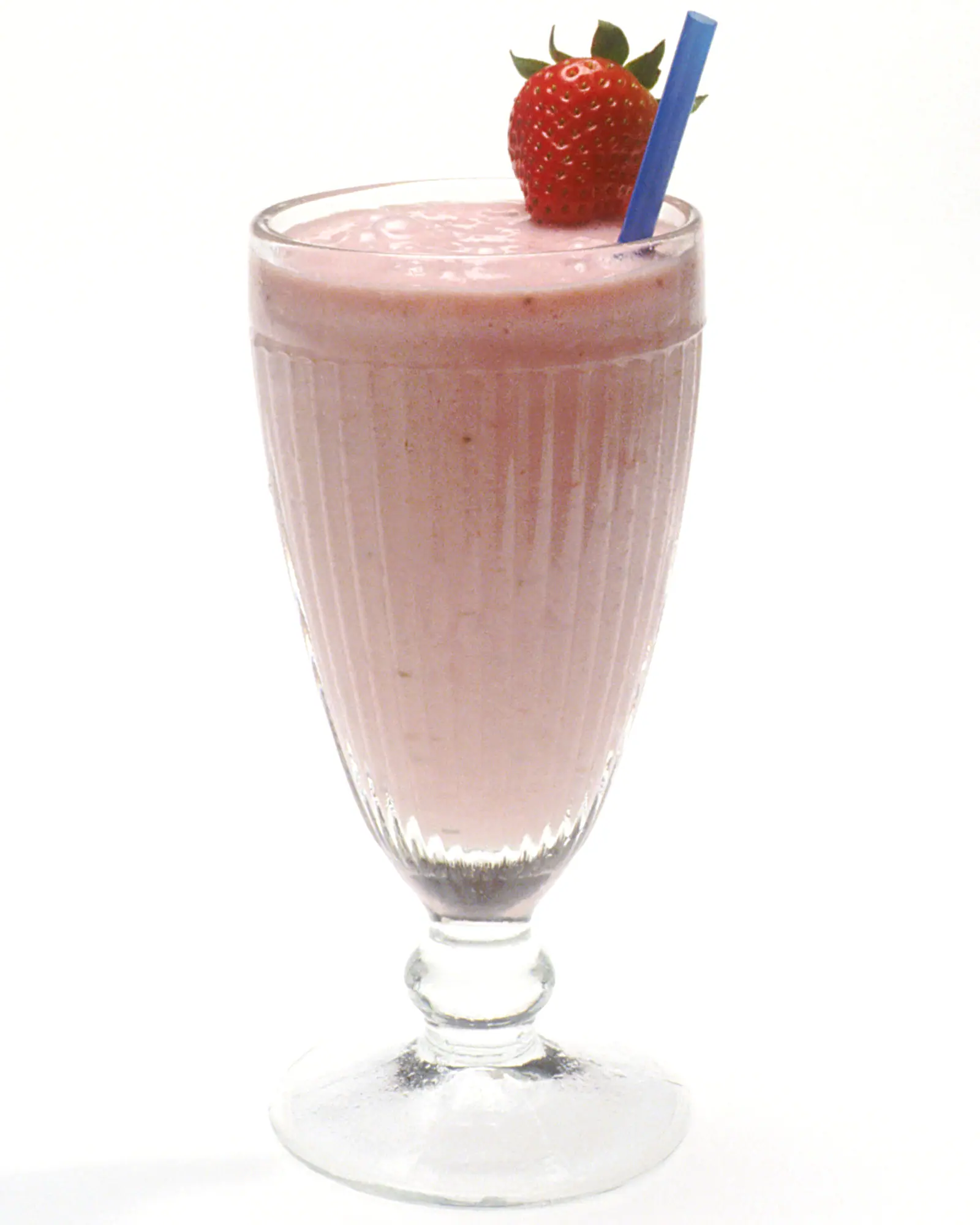 A pink strawberry milkshake in a fluted glass with a straw and a fresh strawberry garnish