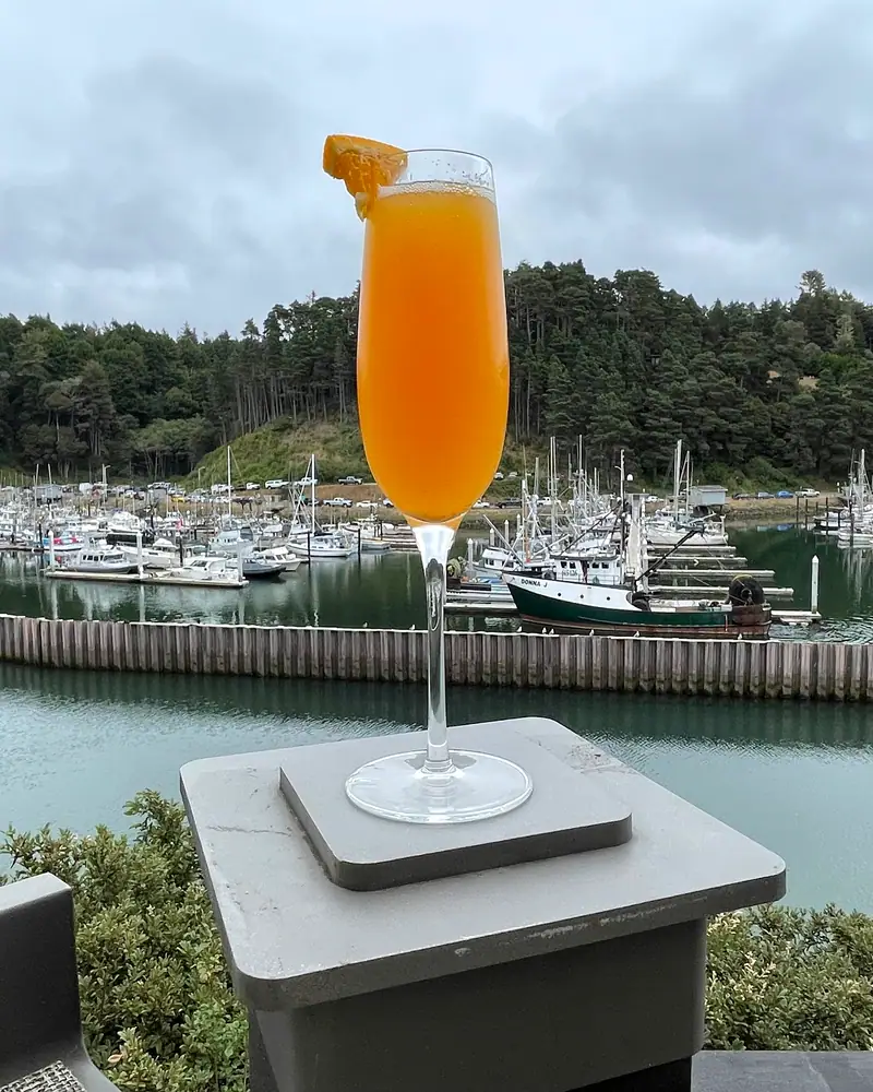 An orange Mimosa in a champagne flute, garnished with a curl of citrus peel, overlooking a harbour