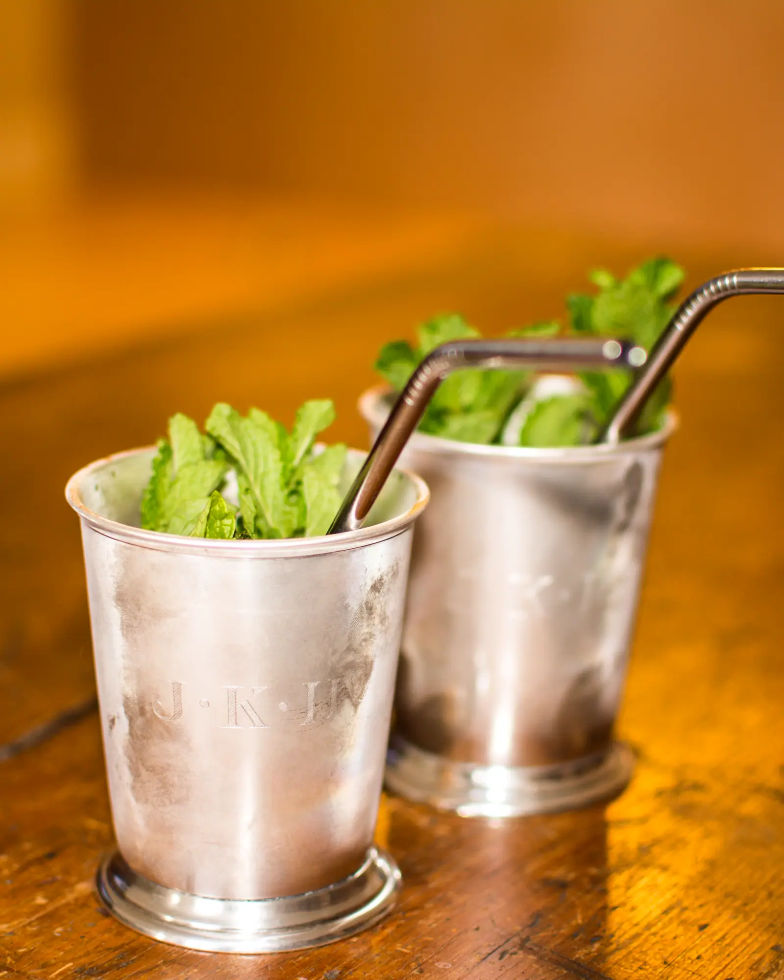 Two Mint Juleps in frosted silver julep cups, packed with crushed ice, mint and metal straws