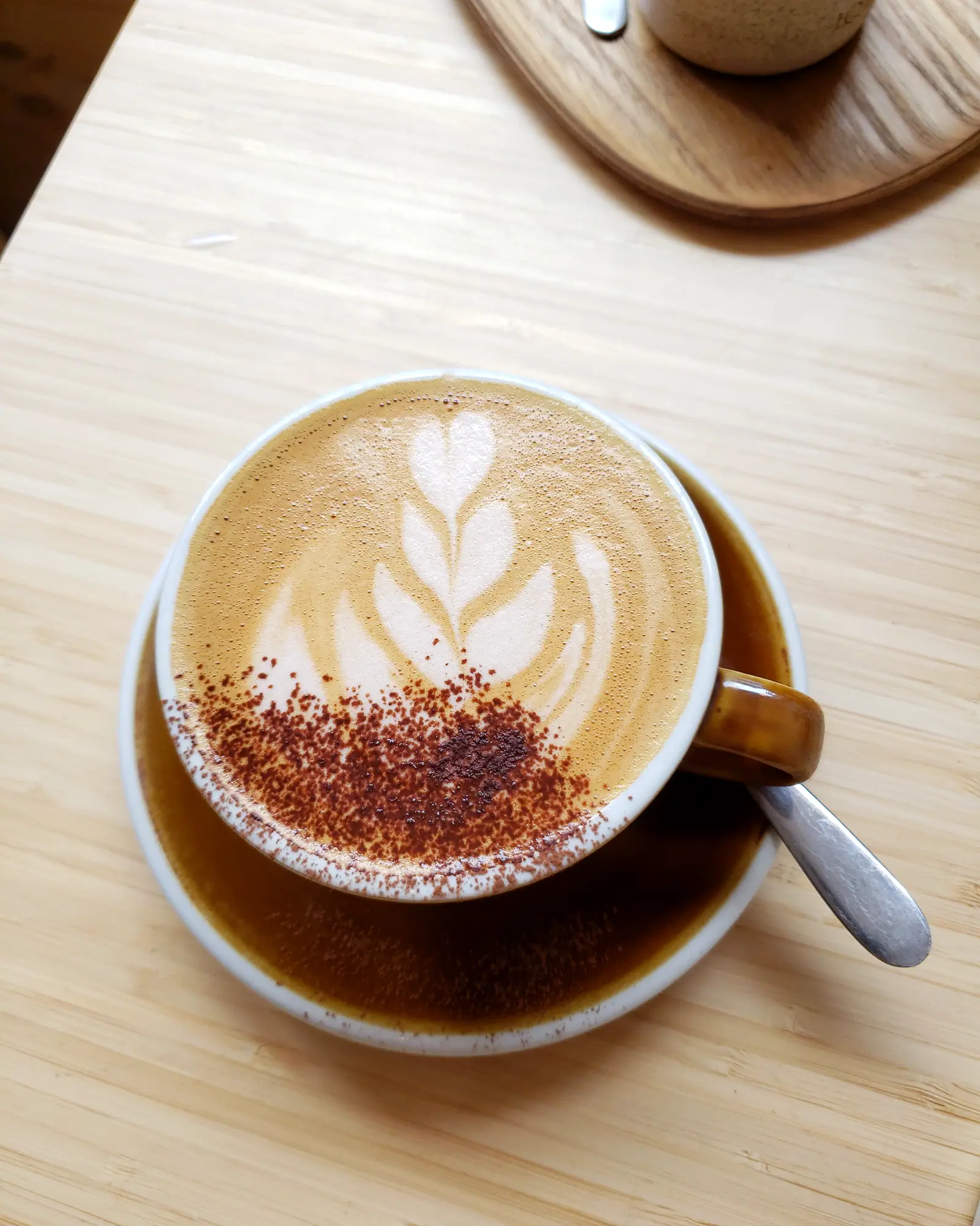 A mocha viewed from above in a cup, latte art and cocoa dusting on the foam, a spoon on the saucer