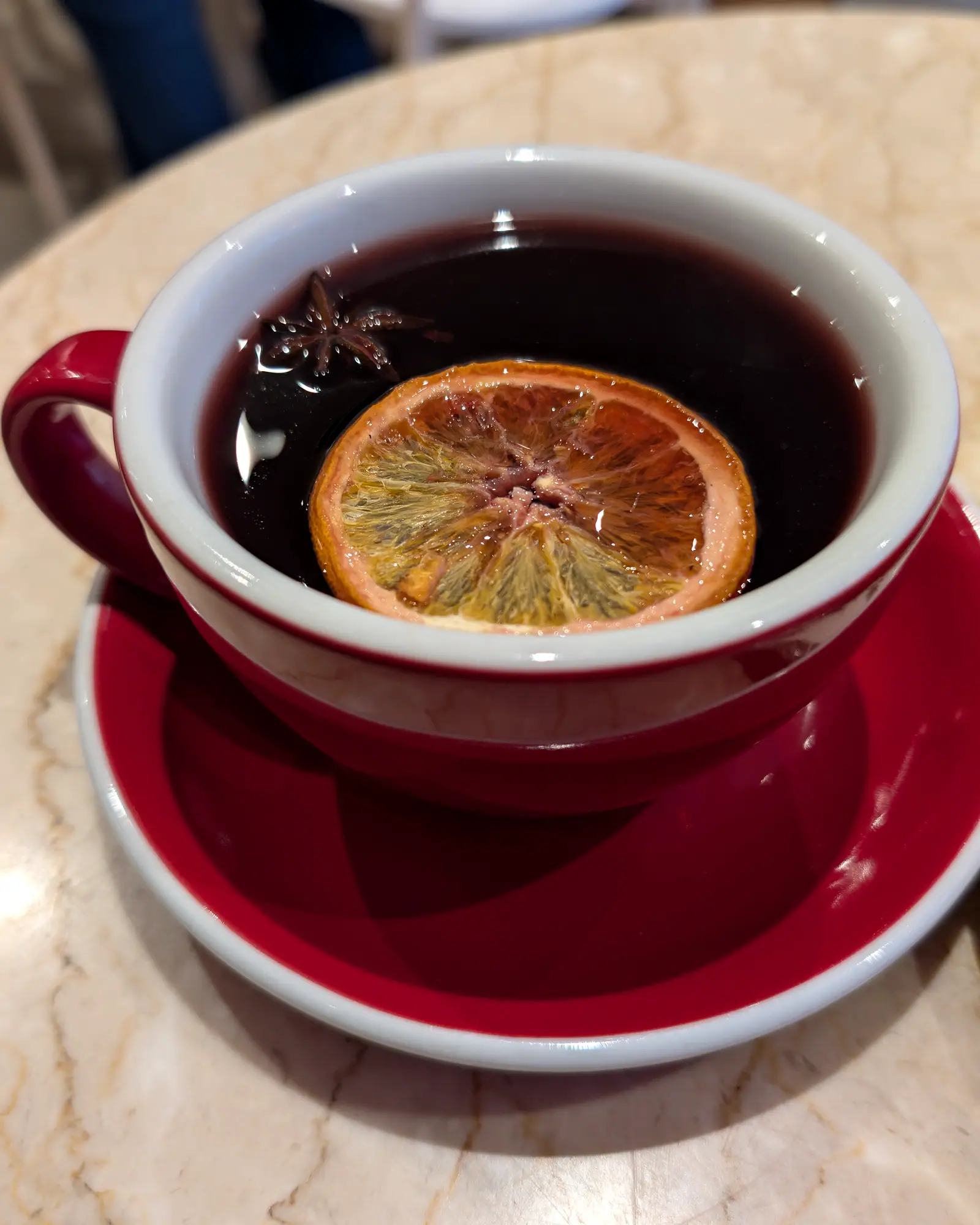 A mug of dark red mulled wine garnished with an orange slice and star anise