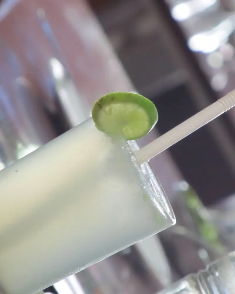 A tall glass of pale, cloudy nimbu pani with a lime slice on the rim and a straw