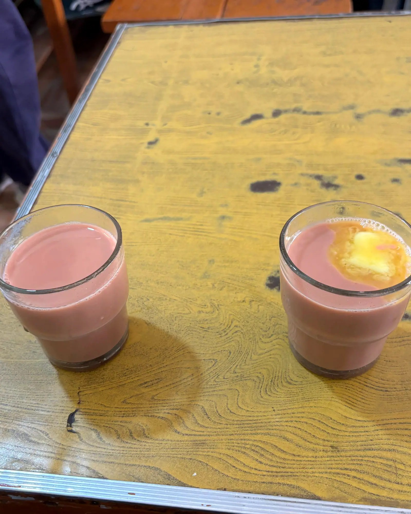 Two glasses of pink Kashmiri noon chai, one topped with a knob of butter