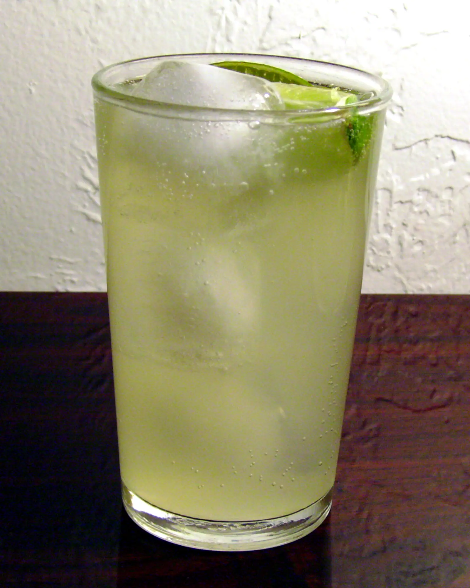 A Paloma in a tall glass over ice, pale yellow-green, garnished with a lime wedge on the rim