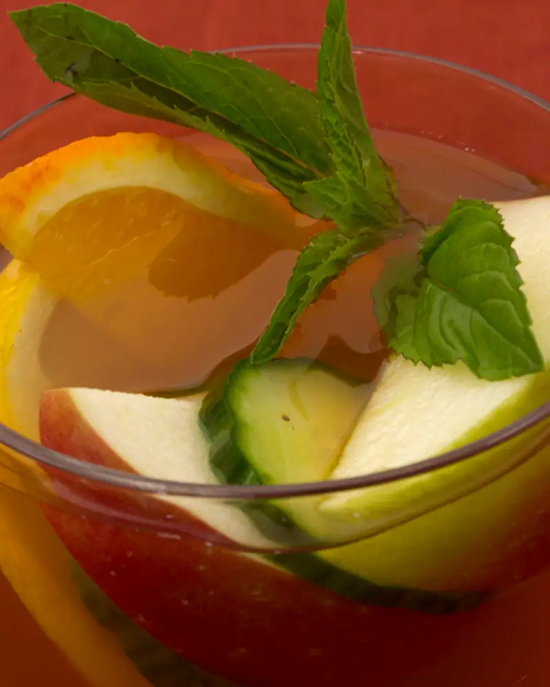 Close overhead view of a Pimm's Cup with mint, cucumber, orange and apple pieces floating in the glass