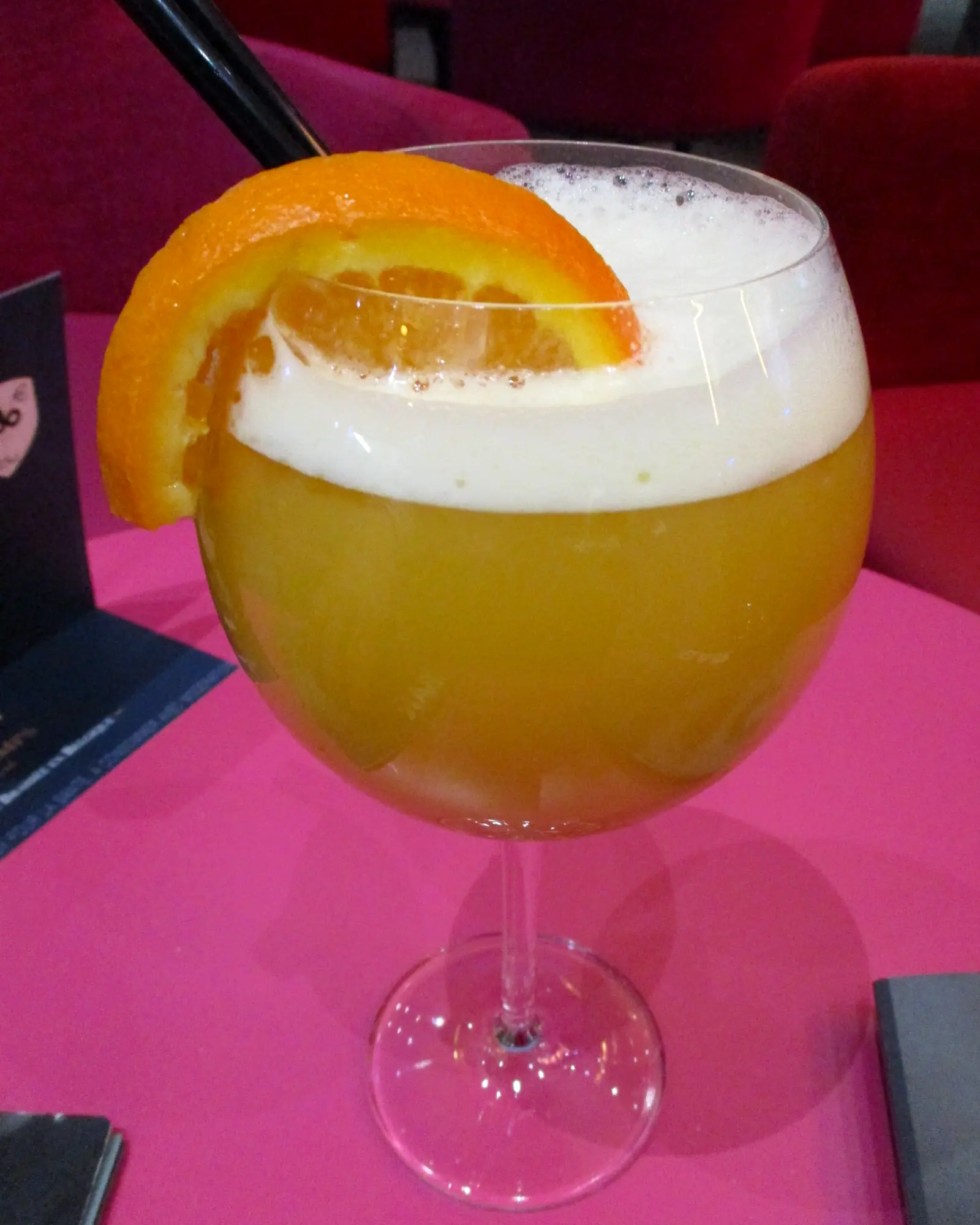 An orange Planter's Punch in a large glass, topped with white foam and garnished with an orange wheel