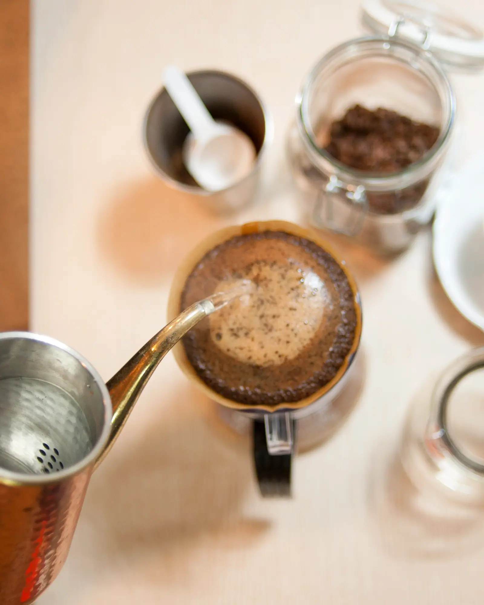 Water poured from a gooseneck kettle onto a bed of coffee grounds in a cone dripper set over a mug, seen from above