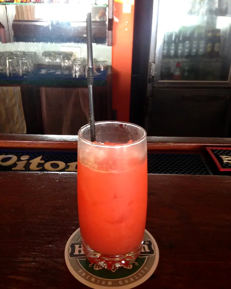 An orange-red rum punch over ice in a tall collins glass with a straw