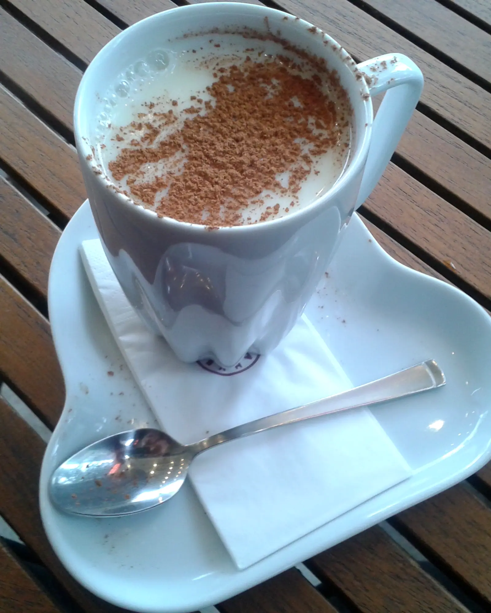A white mug of salep, warm milky drink with a thick dusting of cinnamon across the surface, on a saucer with a spoon