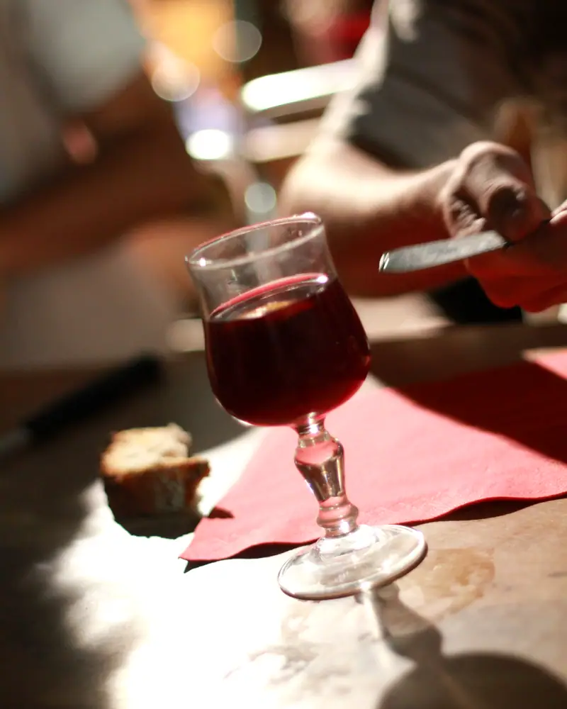 A stemmed red wine glass filled with dark red sangria, on a red napkin with bread nearby